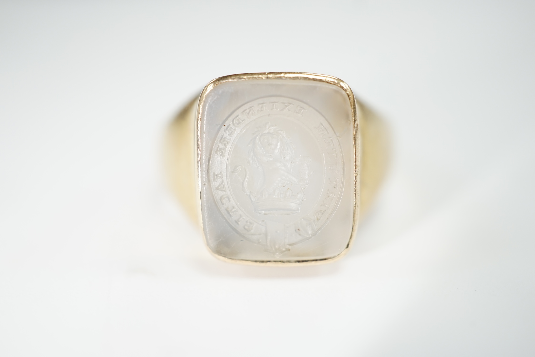 An early 20th century yellow metal and white chalcedony intaglio ring, the matrix carved with the motto 'Virtutum Extendere Factis' with crest, size W, gross weight 9.4 grams.